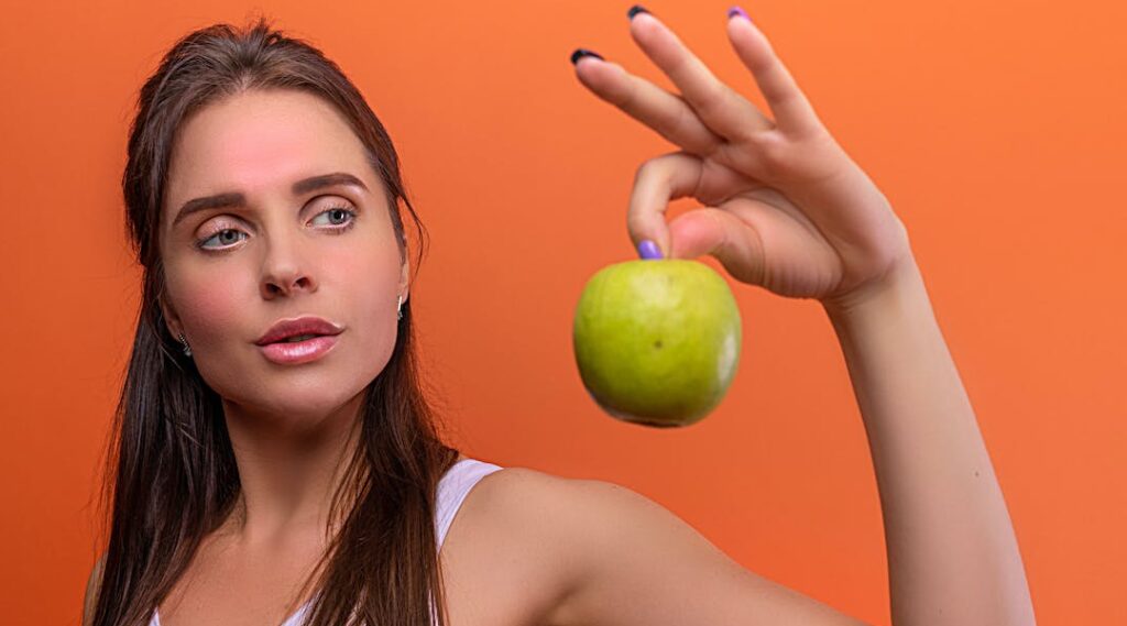 Une femme sportive tenant une pomme du bout des doigts